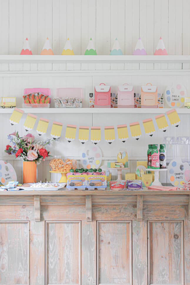 Pastel-colored party setup with decorations and snacks on a wooden shelf.