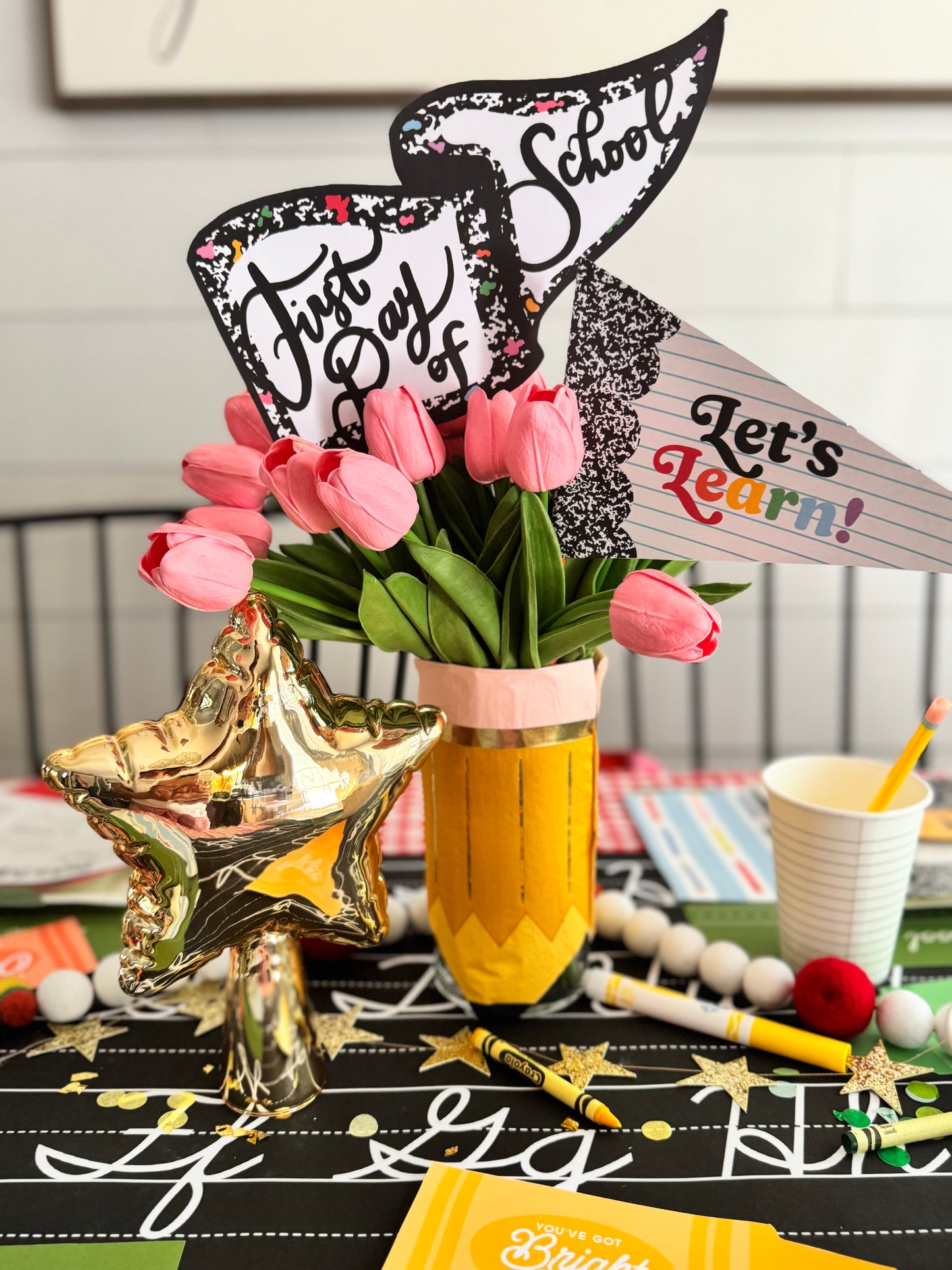 Decorative setup with pink tulips, 'First Day of School' sign, and star-shaped vase on a table.