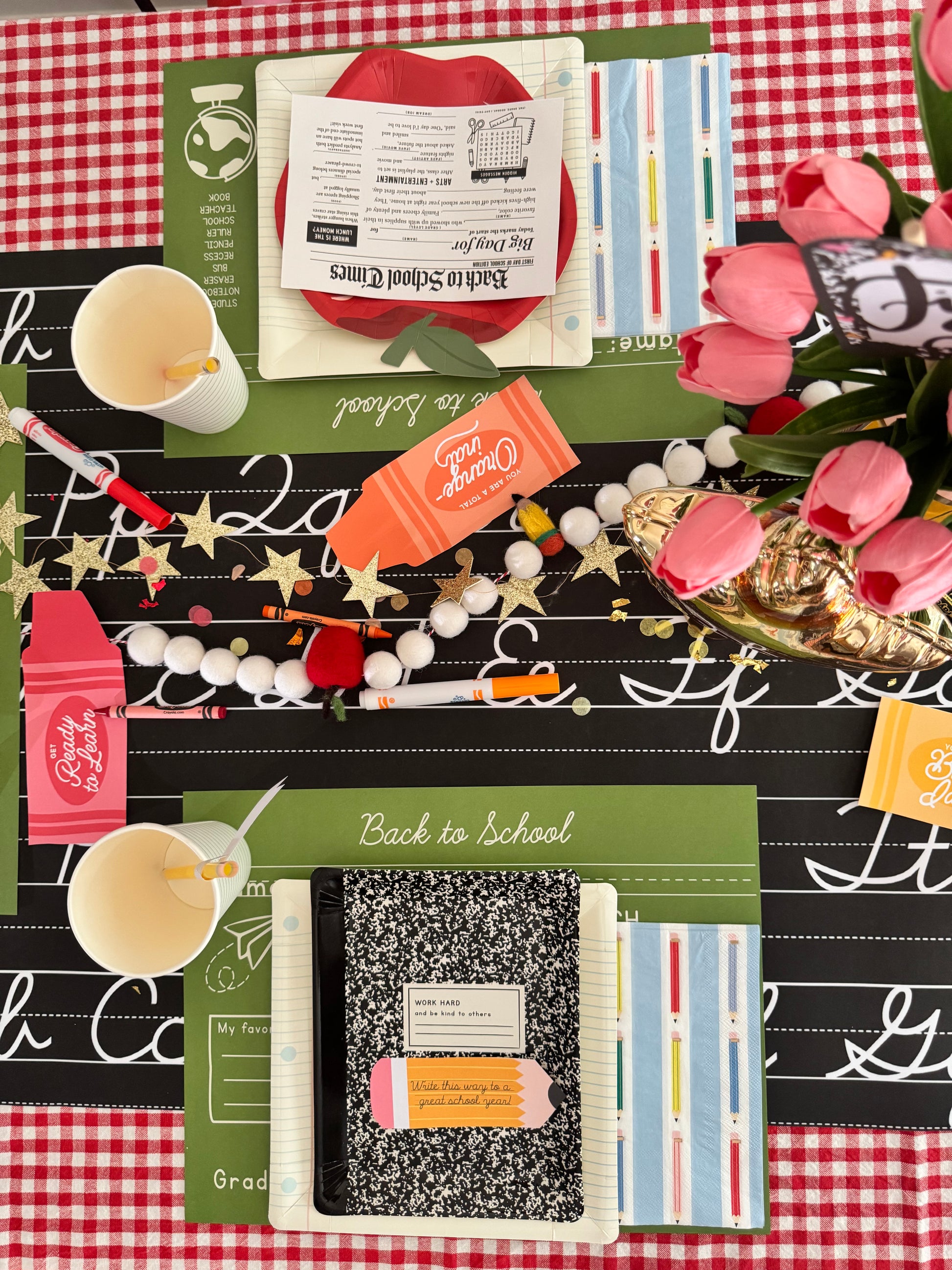 Back-to-school-themed table setting with notebooks, crayons, and decorative elements on a checkered tablecloth.