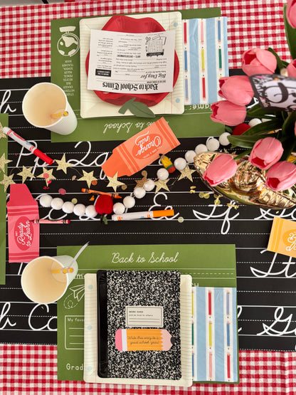 Back-to-school-themed table setting with notebooks, crayons, and decorative elements on a checkered tablecloth.