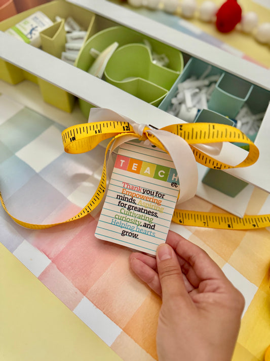 Hand holding a colorful TEACH printable card with text, surrounded by educational materials on a checkered surface.